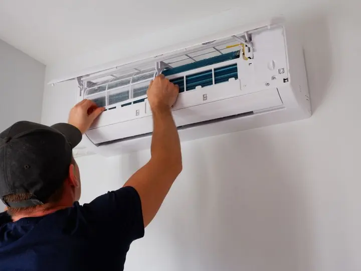 Técnico abrindo a tampa de um ar-condicionado split para a limpeza